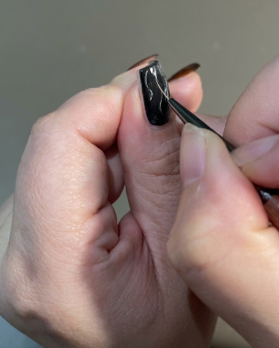 Primer plano de un pincel delineador afinando los extremos de los diseños de llama en una uña para crear un acabado afilado e irregular.