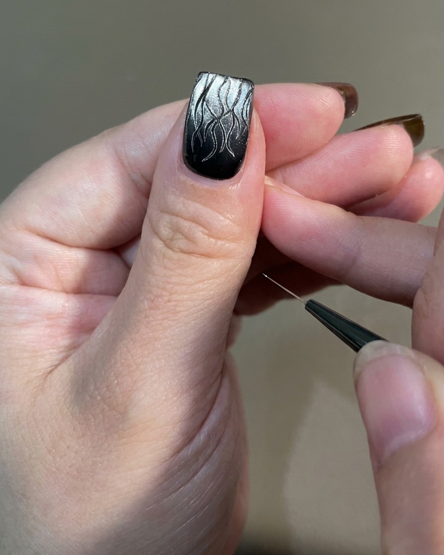 Una mano con el arte de uñas de llama terminado siendo colocada bajo una lámpara de uñas UV profesional para el curado.