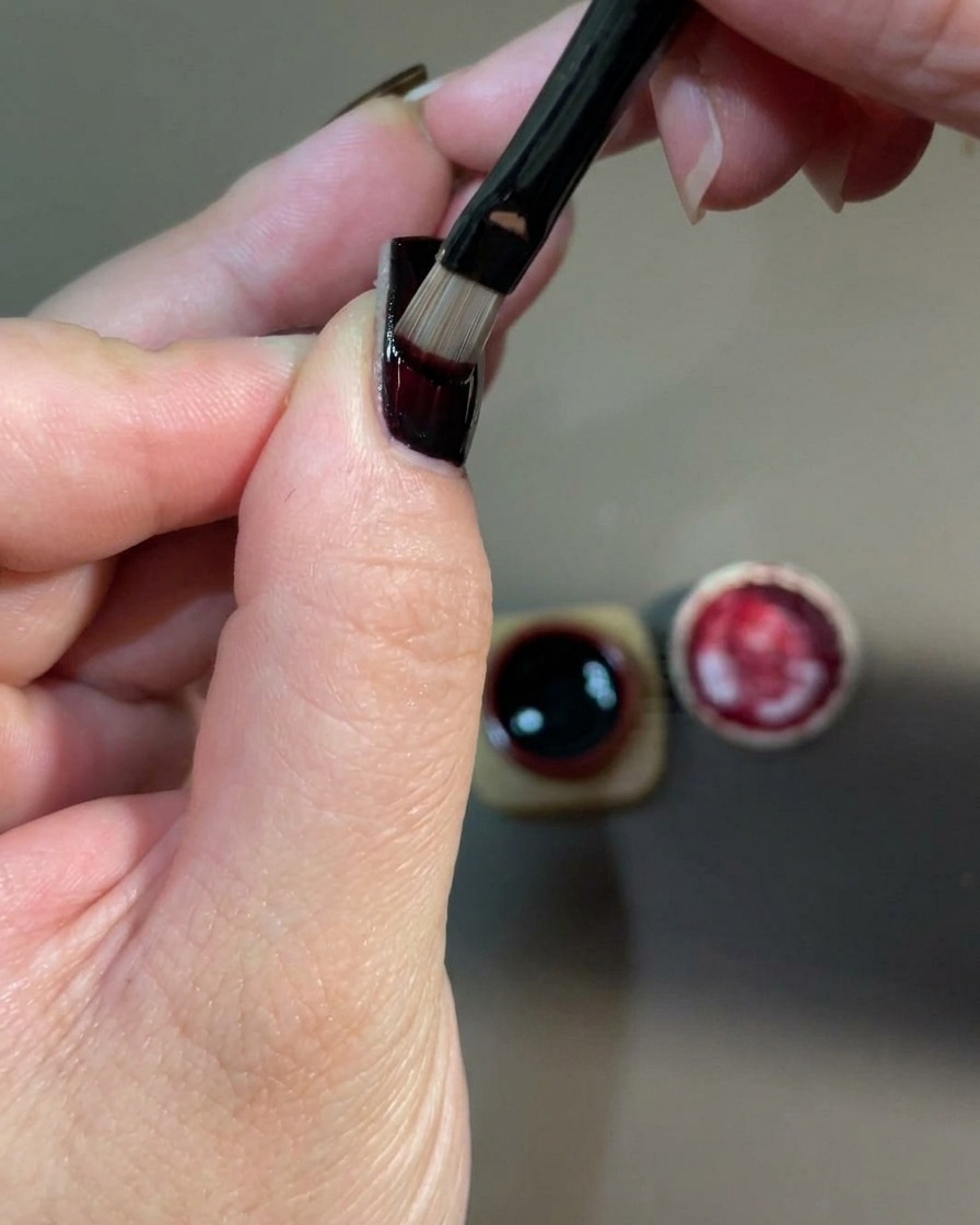Primer plano de una mano colocada dentro de una lámpara de uñas UV para curar la capa de gel rojo recién aplicada.