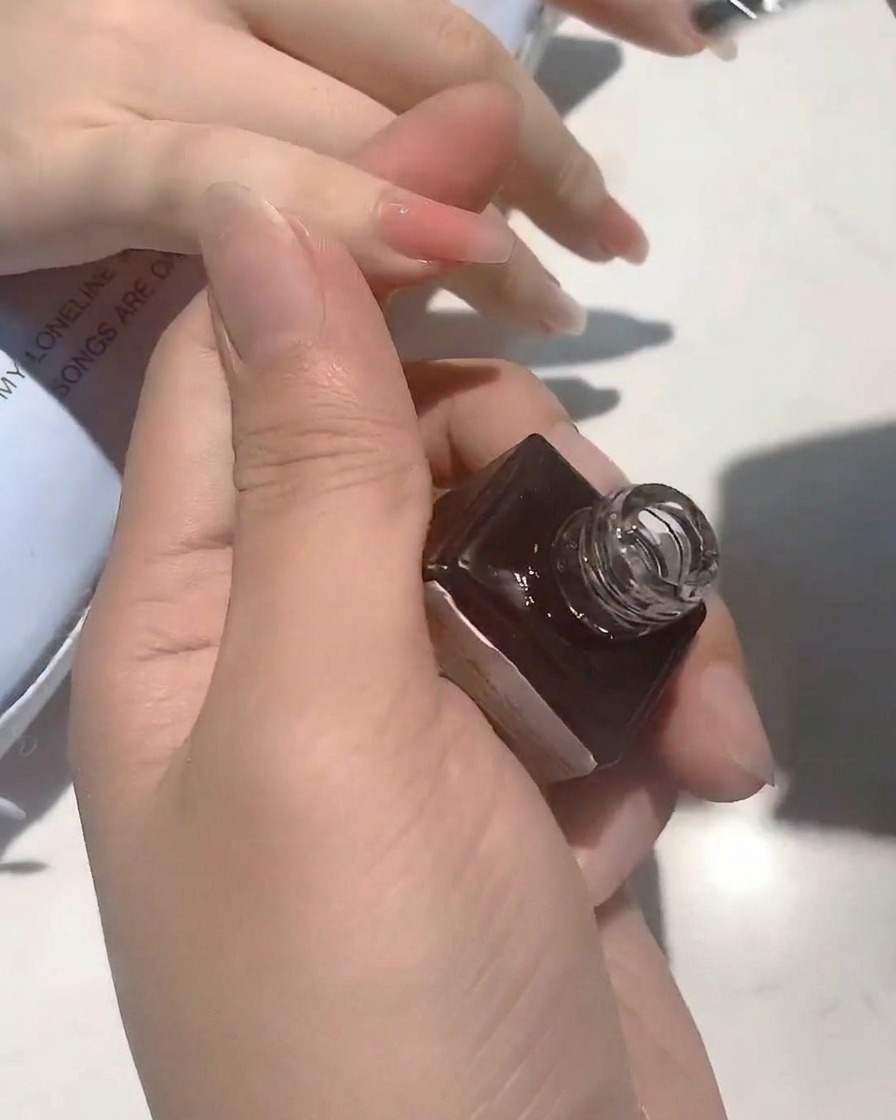 Primer plano de un pincel aplicando un top coat transparente y brillante sobre una uña en tono nude.
