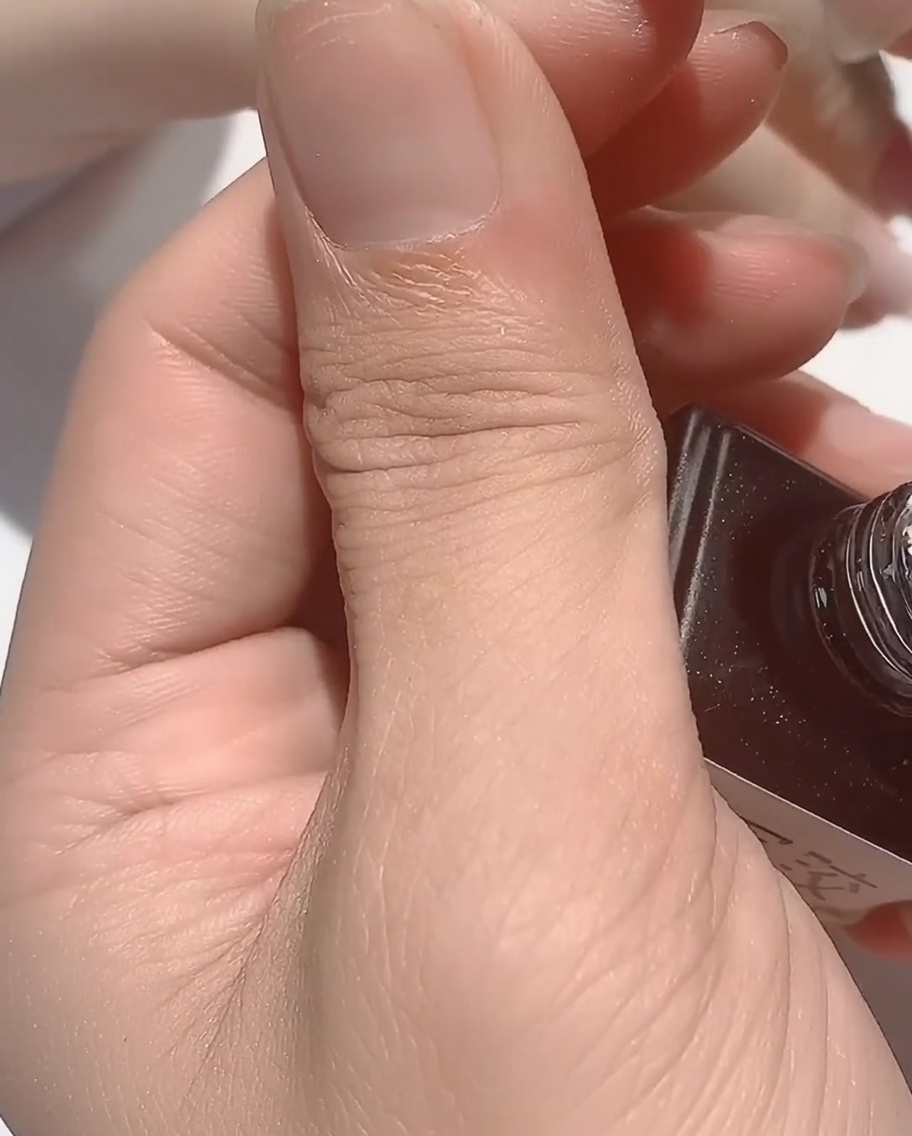 Un pincel aplicando una capa de base rubber transparente y viscosa sobre una uña con detalles iridiscentes.