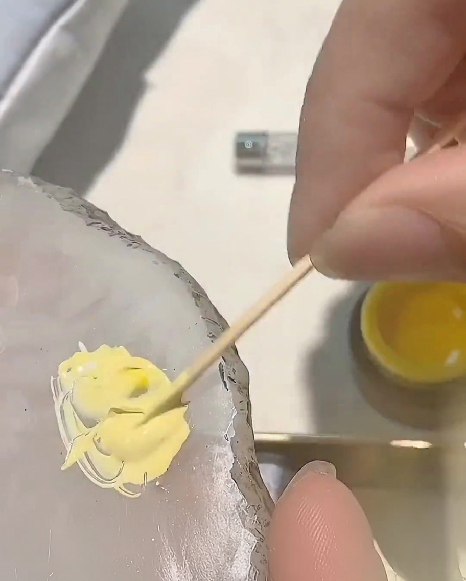 Se añade una pequeña gota de esmalte de gel rojo a la mezcla de gel amarillo existente en una paleta.