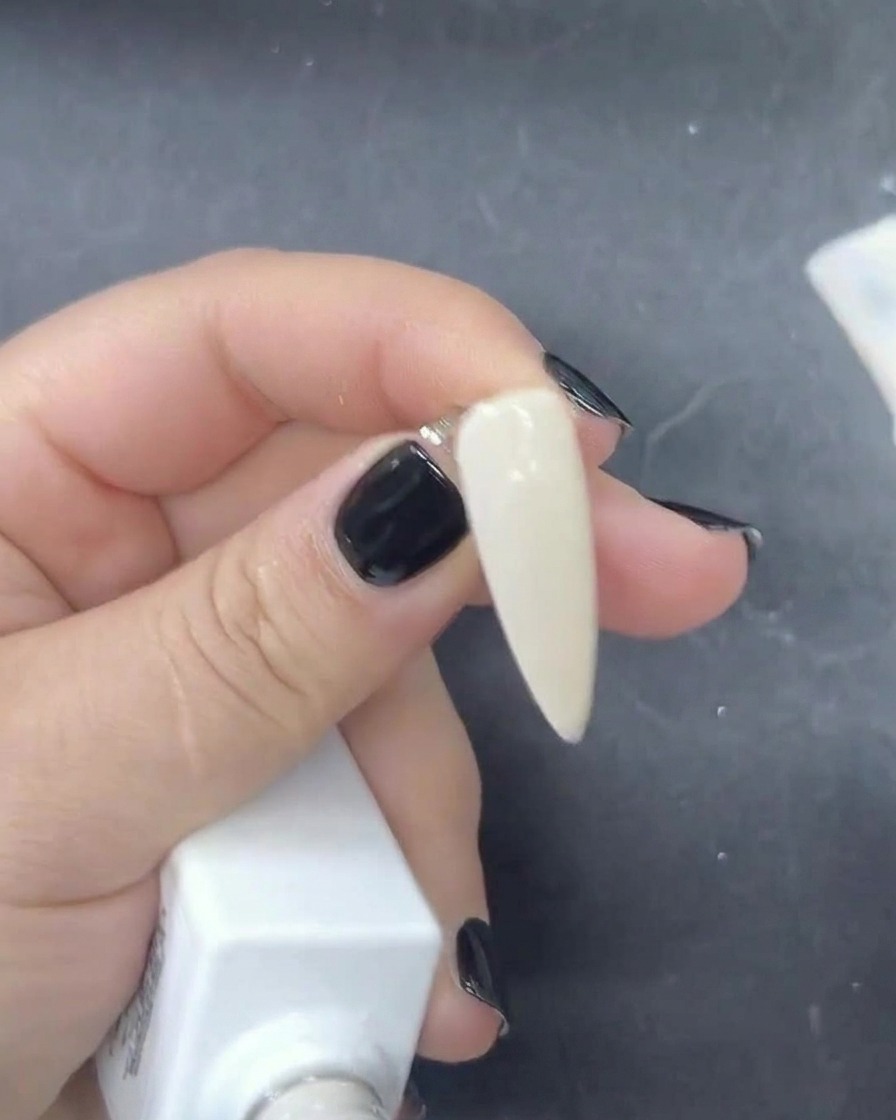 Primer plano de un pincel aplicando gel polish blanco lechoso sobre una uña.