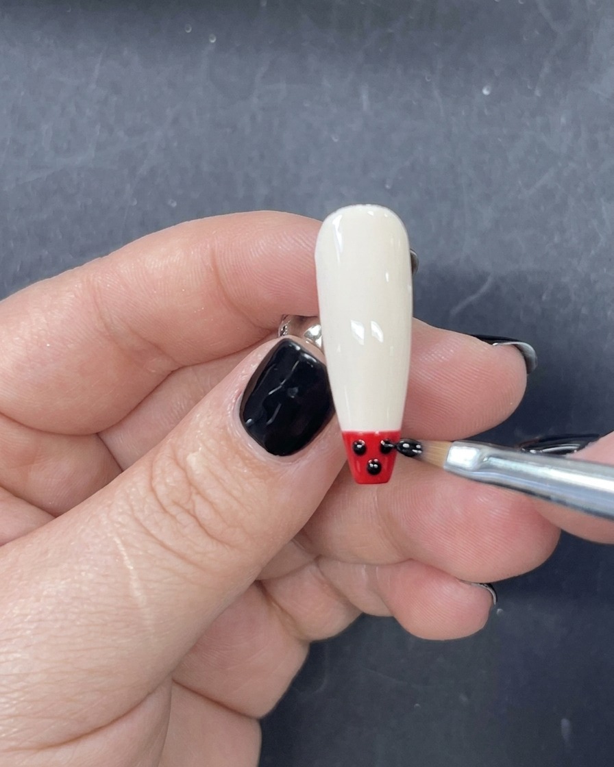 Un pincel delineador fino aplicando una franja horizontal de esmalte de gel rojo justo encima de la punta negra.