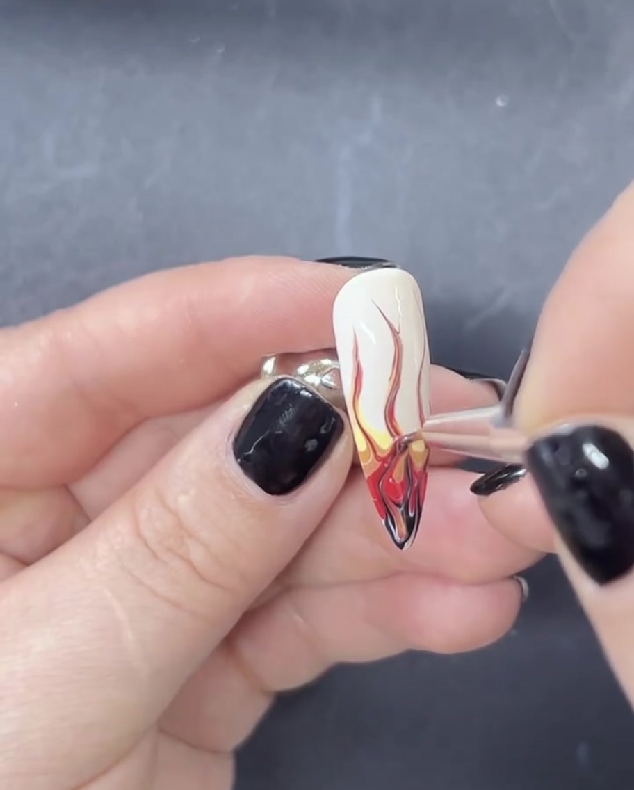 Primer plano de un pincel arrastrando gel rojo y negro hacia arriba sobre una base blanca para crear formas de llama.