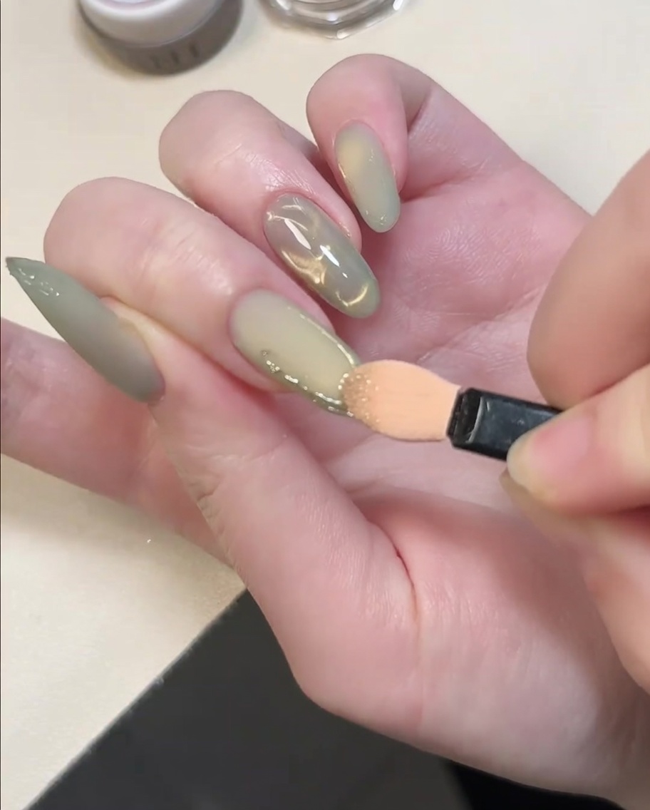 Una punta de aplicador de sombra de ojos frotando polvo de cromo dorado sobre líneas de gel 3D elevadas en una uña.
