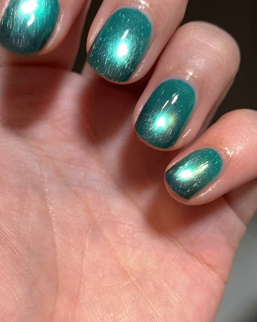 Un pincel aplicando una capa de esmalte en gel ojo de gato verde lago brillante sobre una uña que tiene la punta negra.