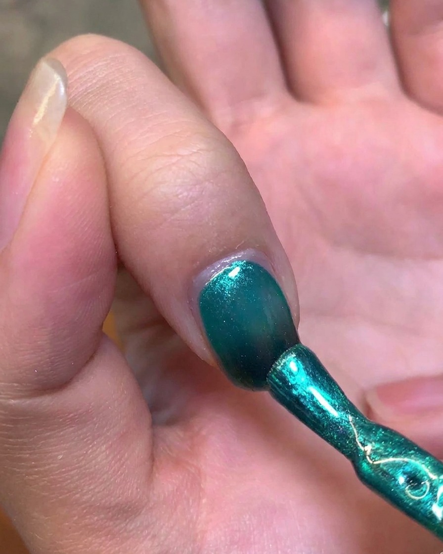 Un imán metálico sostenido cerca del lateral de una uña para manipular el gel verde y crear el destello del ojo de gato.