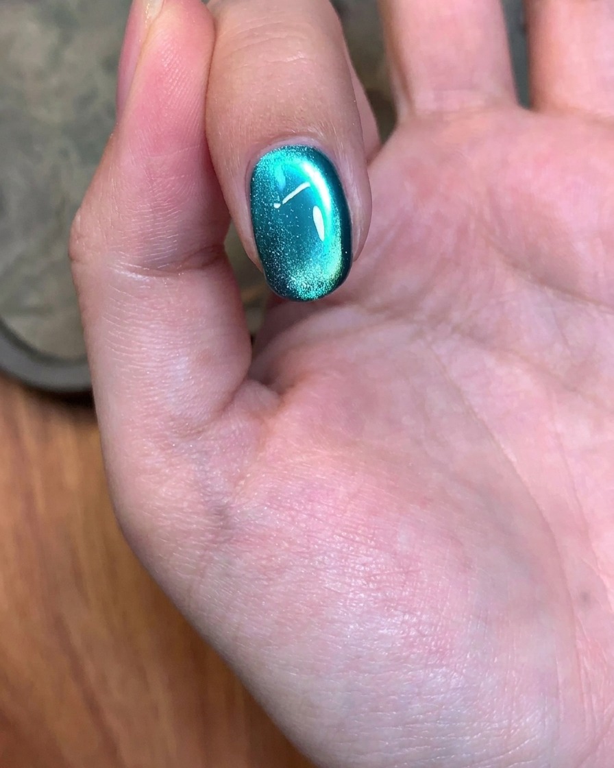 Una herramienta magnética utilizada con movimientos circulares sobre una uña pintada con gel verde para ajustar el brillo.