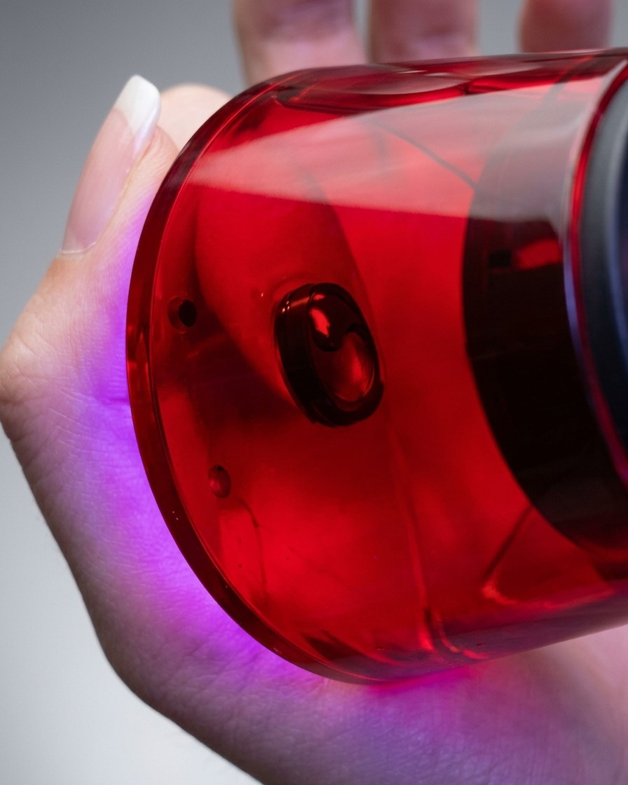 Primer plano de una mano sosteniendo una lámpara UV/LED compacta de color rojo directamente sobre un dedo para curar el esmalte en gel aplicado.