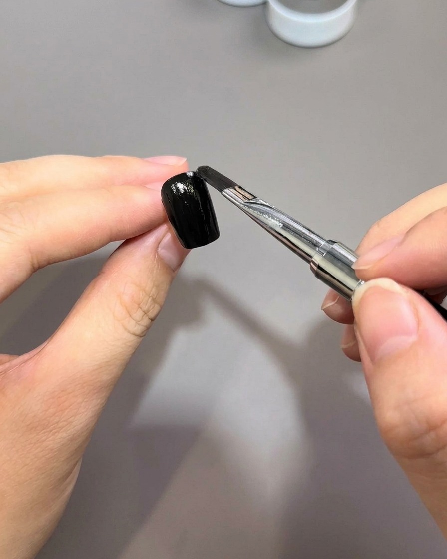 Un pincel aplicando una capa suave de esmalte en gel negro sobre la superficie de una uña preparada.