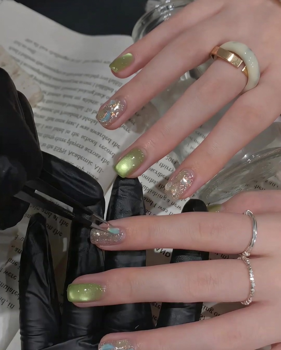 Un pincel aplicando una capa de top coat brillante sobre una uña decorada con piedras.