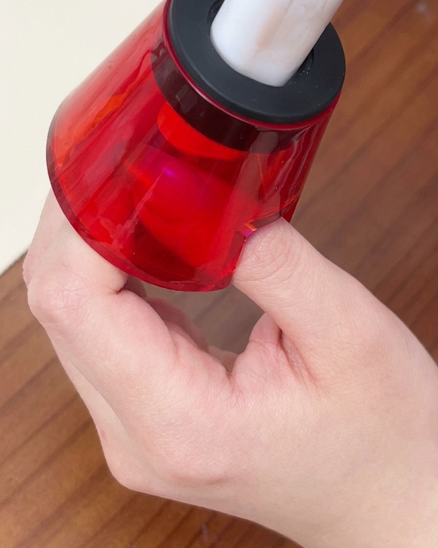 Un dedo bajo una pequeña lámpara LED roja portátil para curar el esmalte en gel.