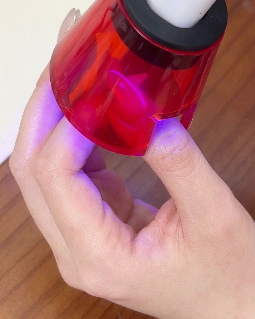 Un dedo curándose bajo una lámpara LED roja portátil para fijar el diseño de gel magnético.