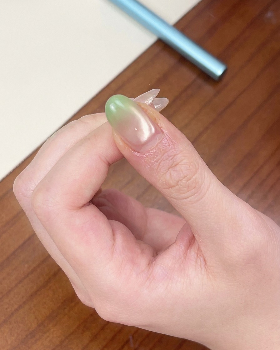 Una uña con punta en degradado verde colocada bajo una mini lámpara UV roja portátil.