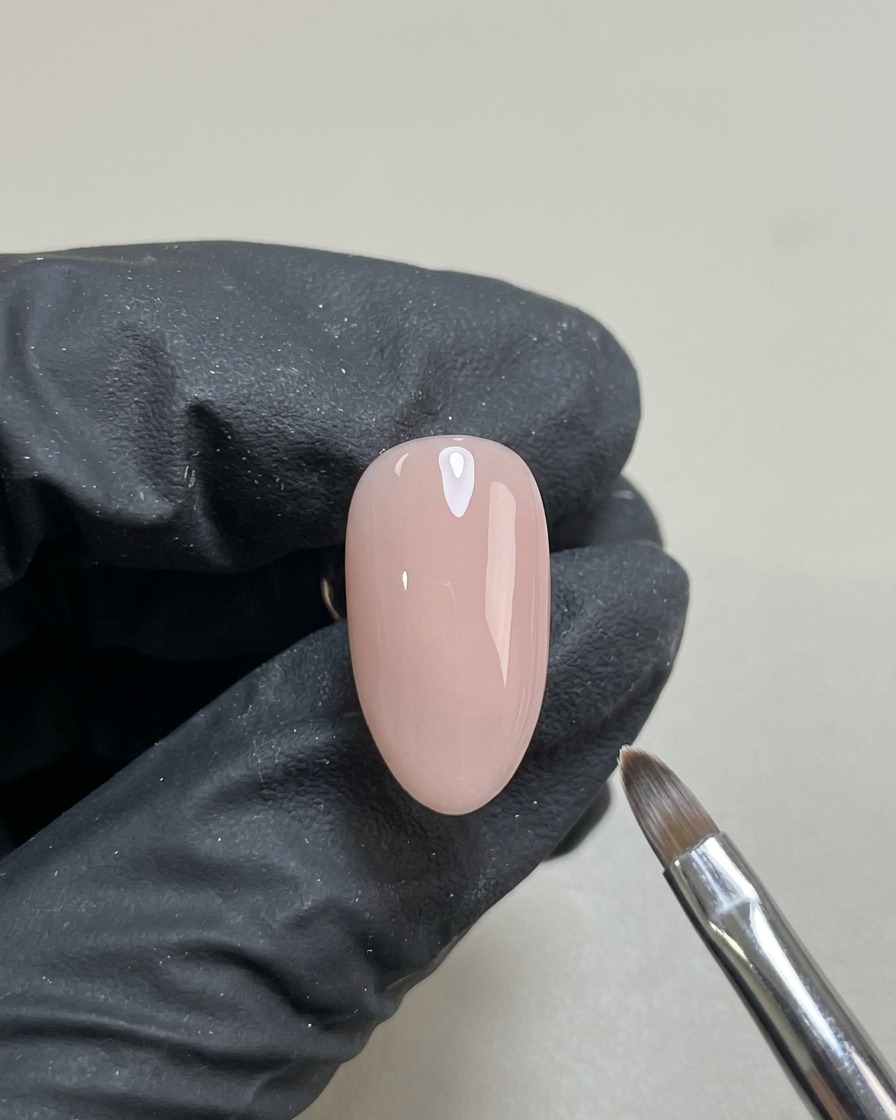Una uña con una base de gel nude translúcida y lisa, curada y lista para el diseño.