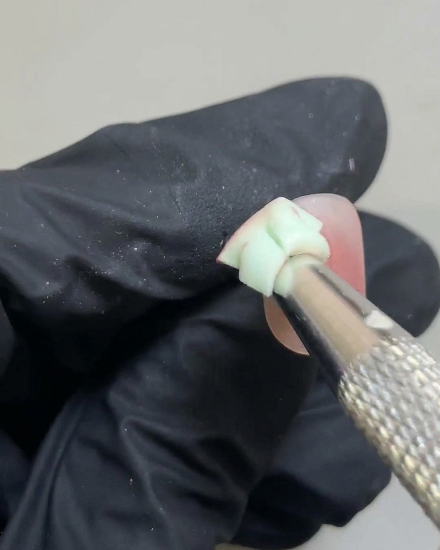 Una pequeña esponja difuminando suavemente los bordes de un punto de gel rosa para crear un degradado blush.