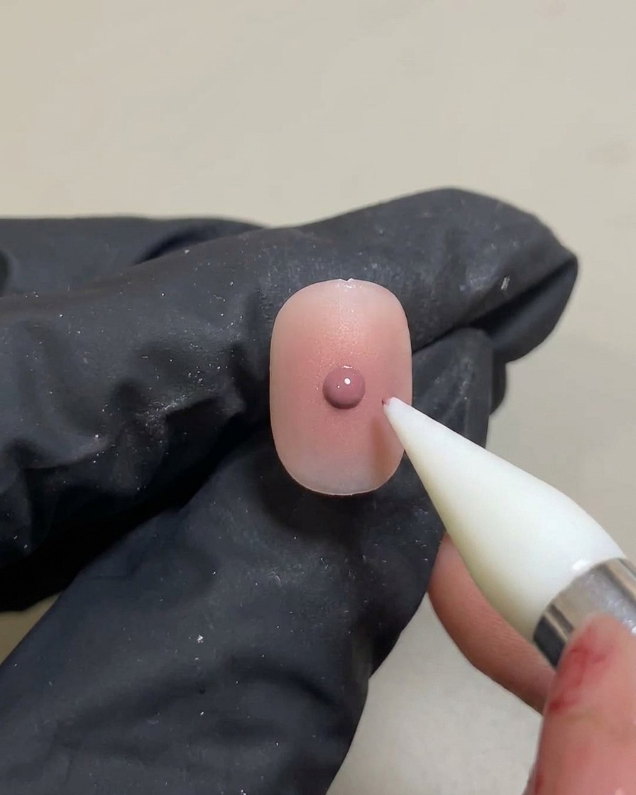 Una herramienta de silicona aplicando un punto pequeño y concentrado de gel rosa sobre un degradado blush ya curado.