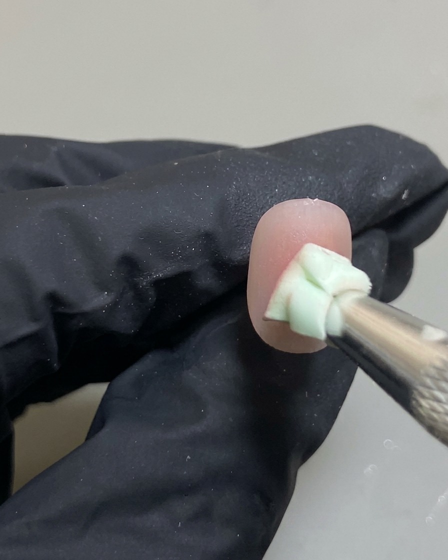 Primer plano de una uña con una esponja difuminando un punto de gel rosa hacia un efecto blush ombré.