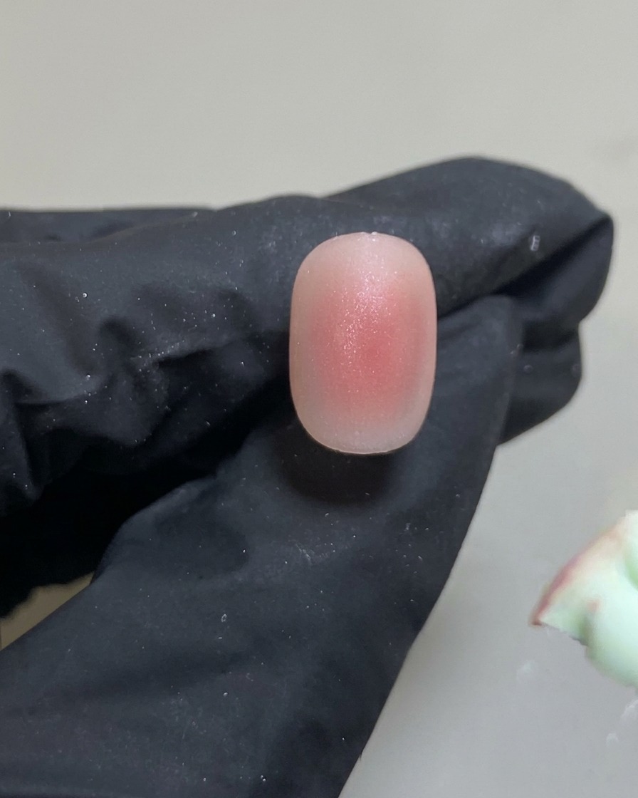 Una herramienta de silicona colocando un punto pequeño y preciso de gel rosa en el centro de la uña.