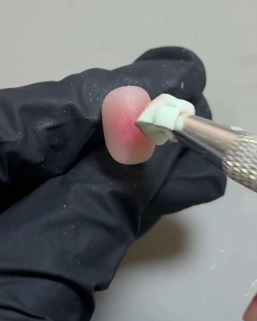 Primer plano de la esponja perfeccionando los bordes del diseño de uñas ombré blush.