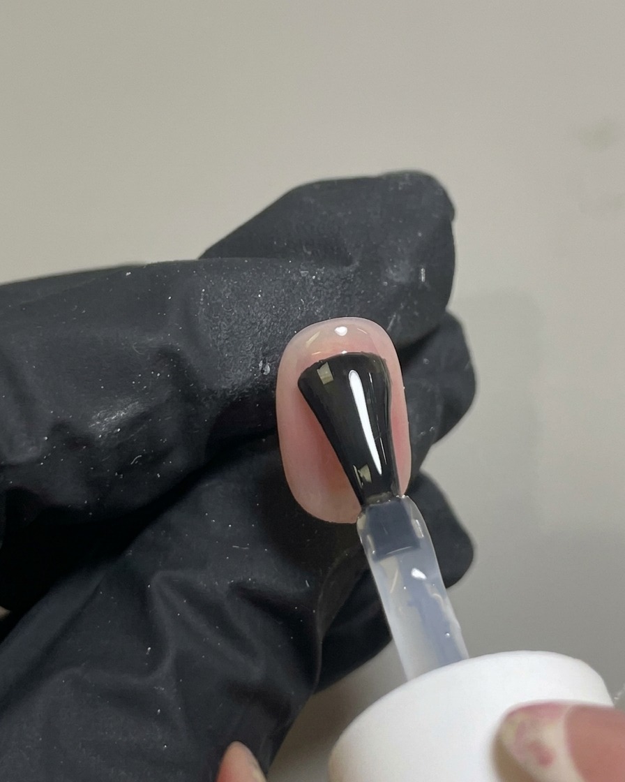 Un pincel aplicando un top coat transparente y brillante sobre el diseño de uñas blush terminado.