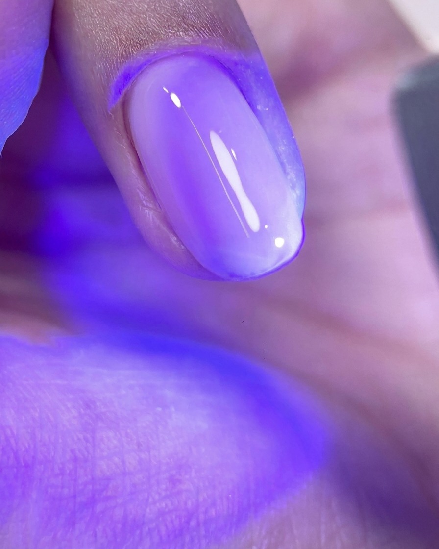 Una uña con una capa de gel rosa brillante sin curar bajo la luz púrpura de una lámpara de curado UV/LED.
