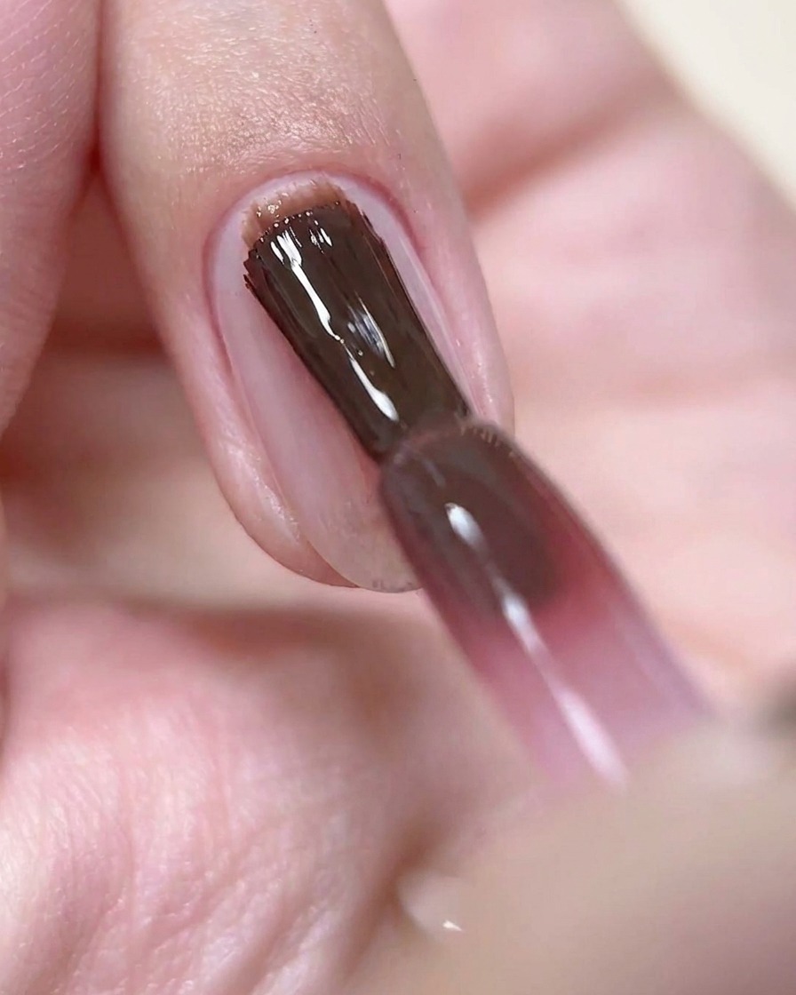 Un pincel de uñas aplicando una capa fina de esmalte de gel color rosa vino profundo sobre una uña preparada.