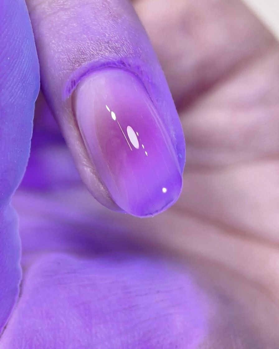 Una uña blush rosa bellamente manicurada curándose bajo la luz púrpura brillante de una lámpara de uñas UV/LED.