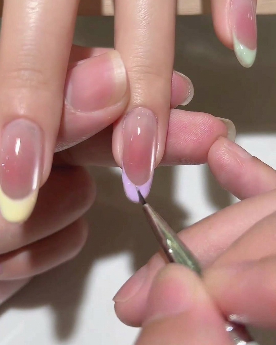 Un pincel aplicando una capa de top coat transparente sobre una manicura francesa terminada.