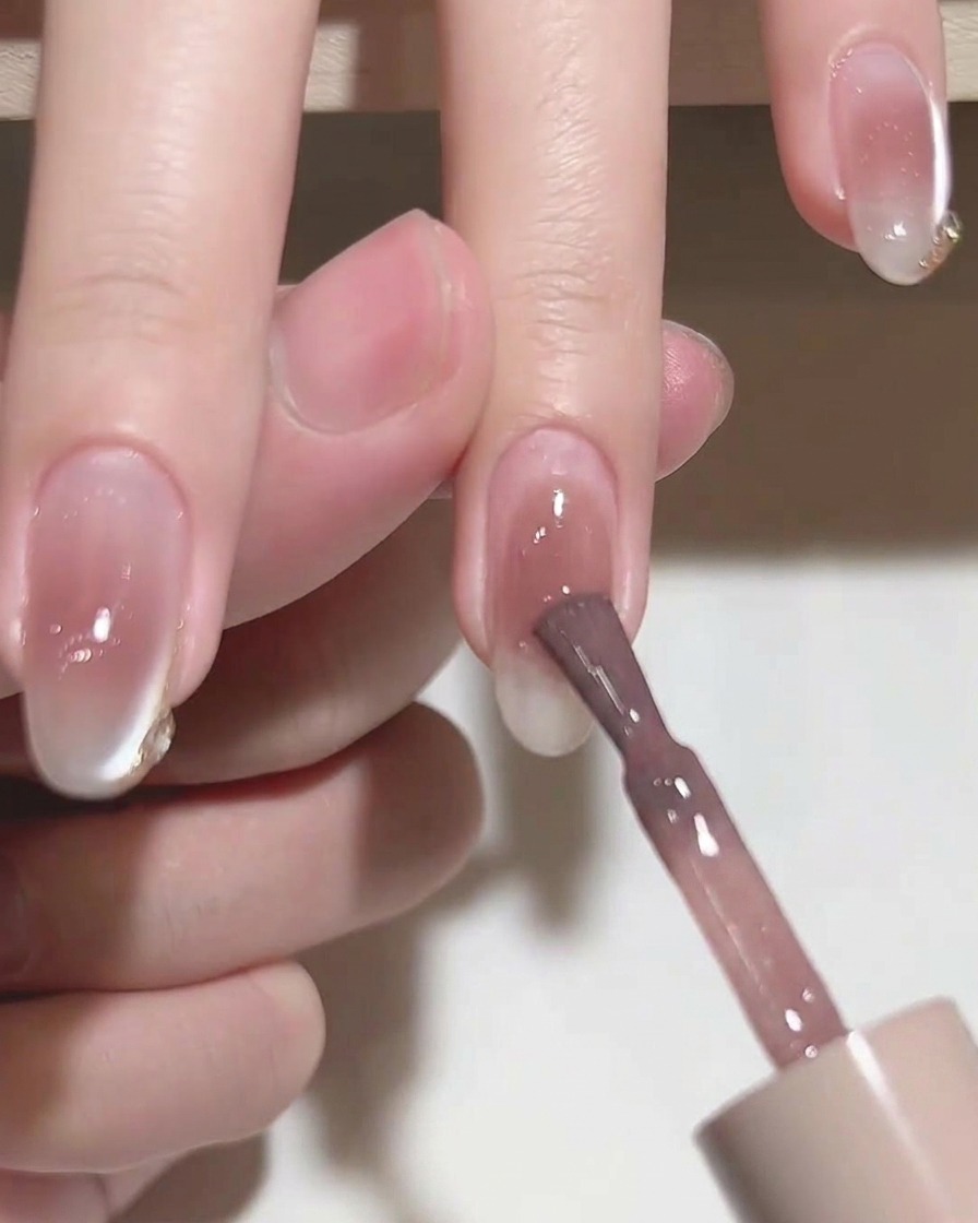 Un pincel plano alisando el esmalte en gel rosa sobre la uña.