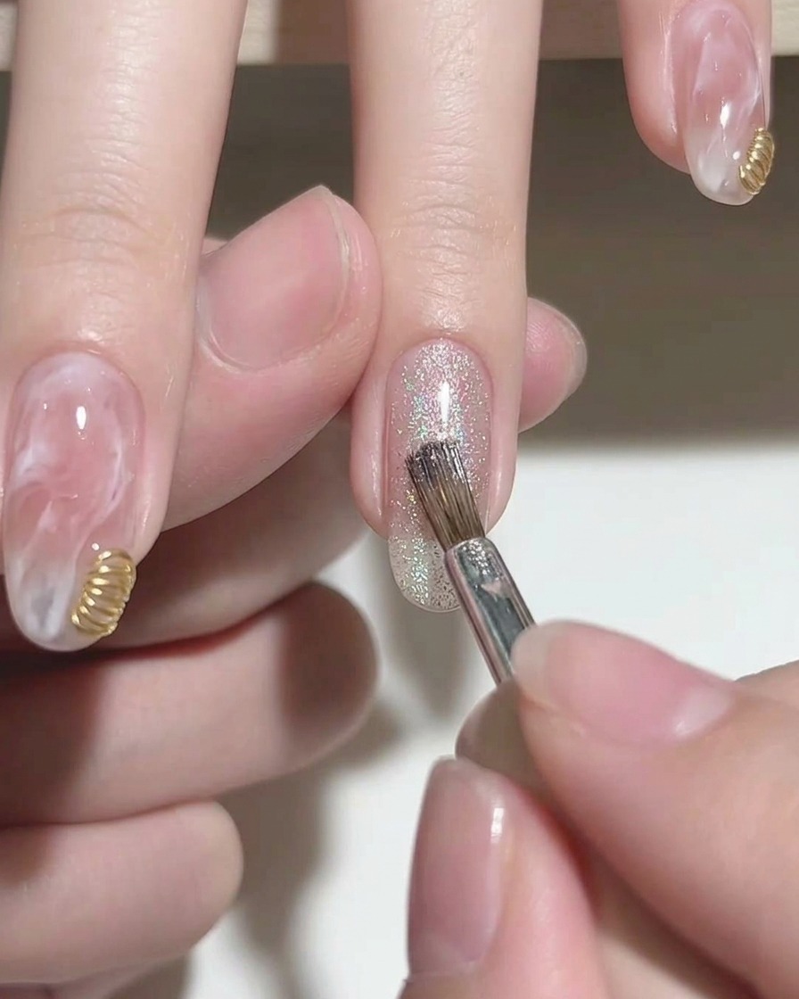 Un pincel aplicando esmalte en gel cat eye plateado brillante en la punta de una uña de gel rosa.