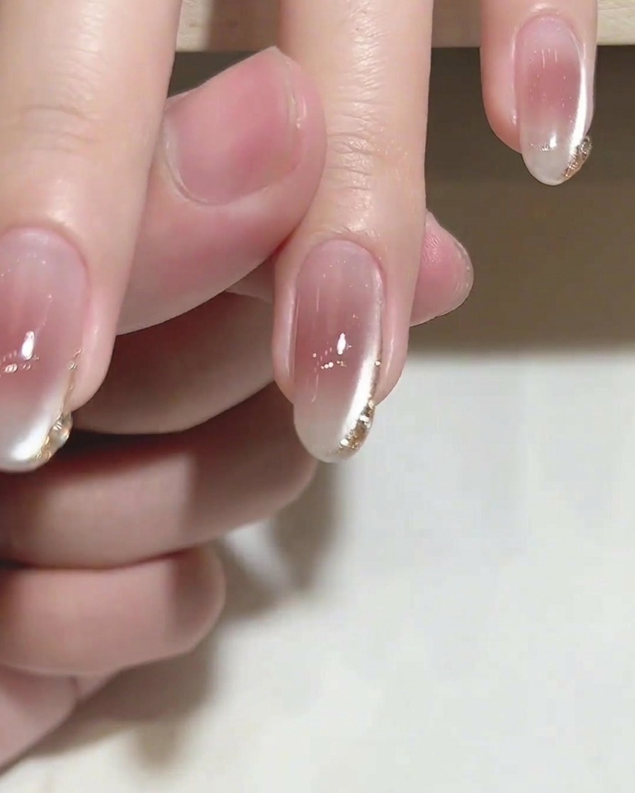 Un pincel aplicando un top coat transparente y brillante sobre una uña con delicados detalles dorados en la punta.