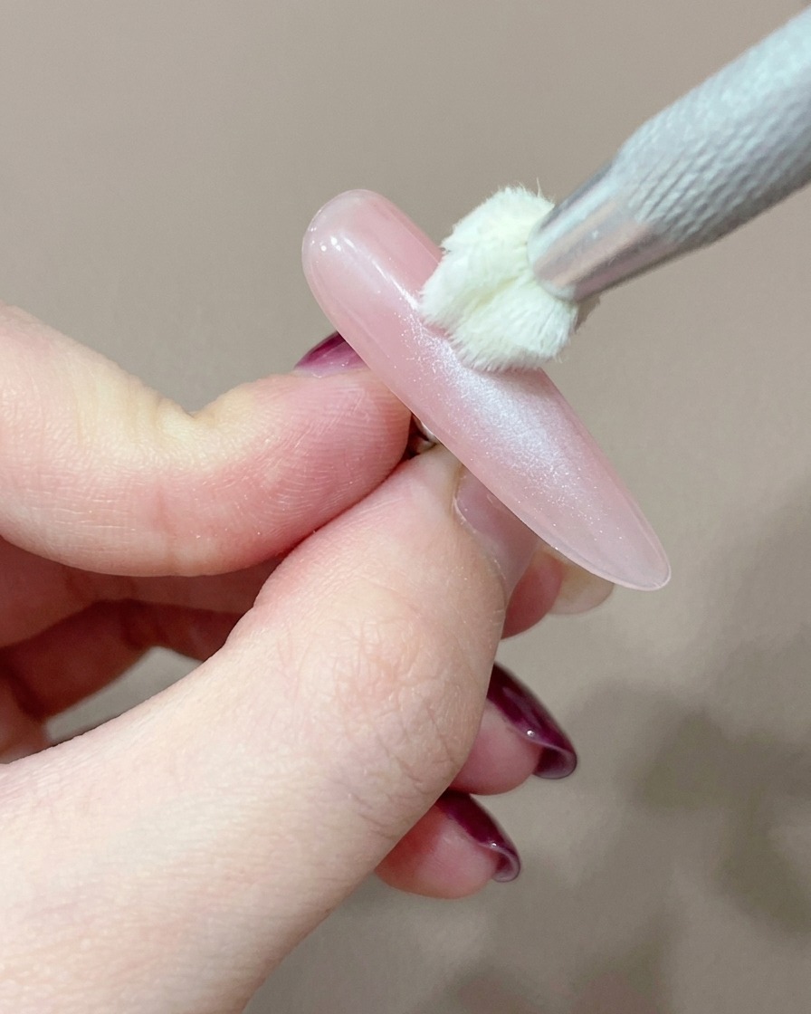 Una herramienta aplicadora de silicona añadiendo cuidadosamente un punto concentrado de gel rosa en el centro de la uña.