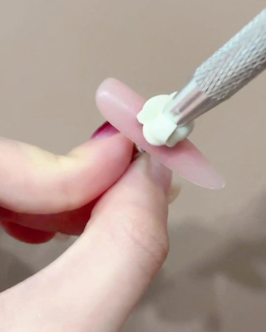 Un pincel aplicando un pequeño y preciso punto de gel blush rosa en el centro de una uña.