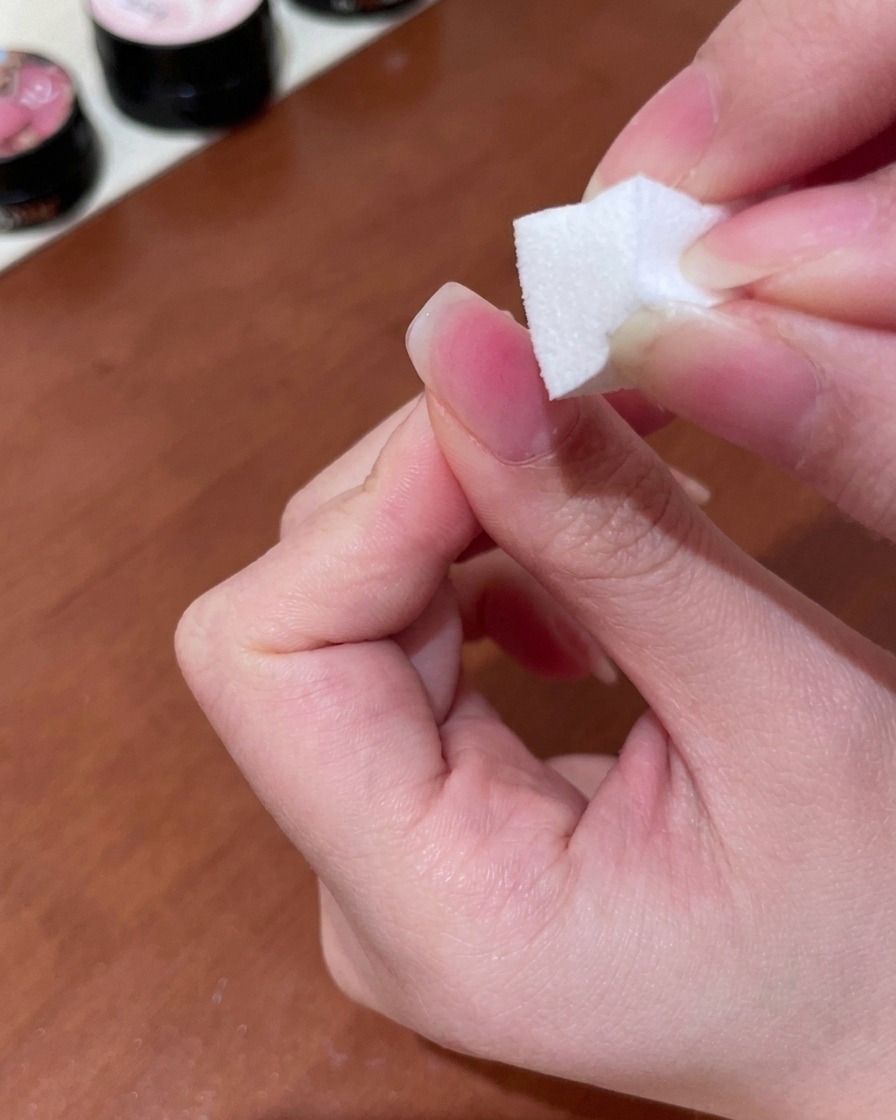 Una esponja de maquillaje utilizada para dar toques y difuminar gel durazno en un degradado suave sobre la uña.