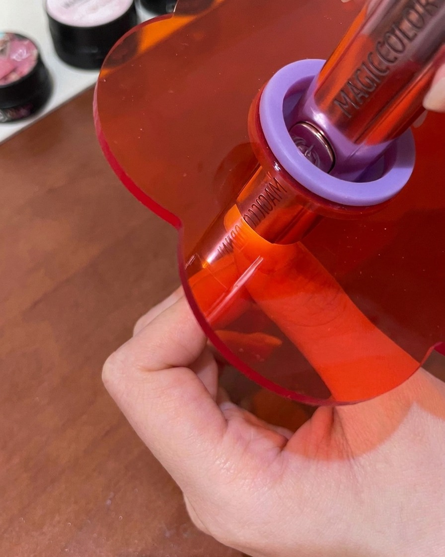 Una uña curándose bajo una pequeña lámpara UV/LED rosa de mano.