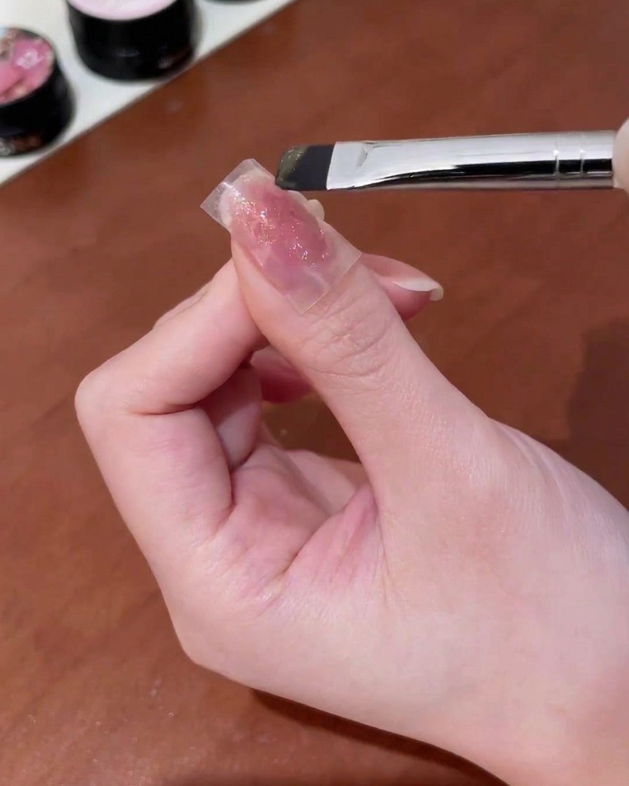 Un pincel aplicando gel ojo de gato dorado sobre una pegatina de mariposa en una uña.
