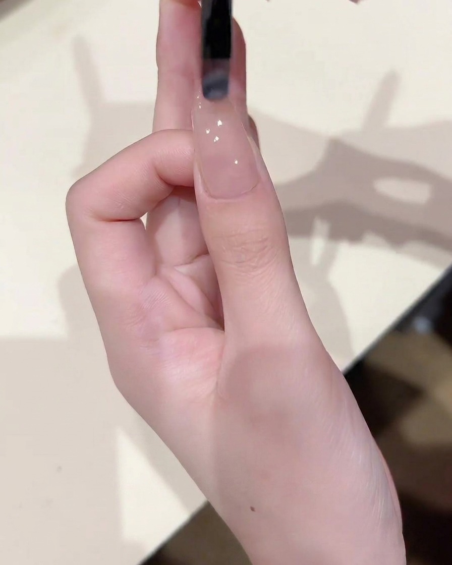 Primer plano de un pincel aplicando una capa fina y uniforme de gel nude translúcido sobre una uña que ya tiene una base.
