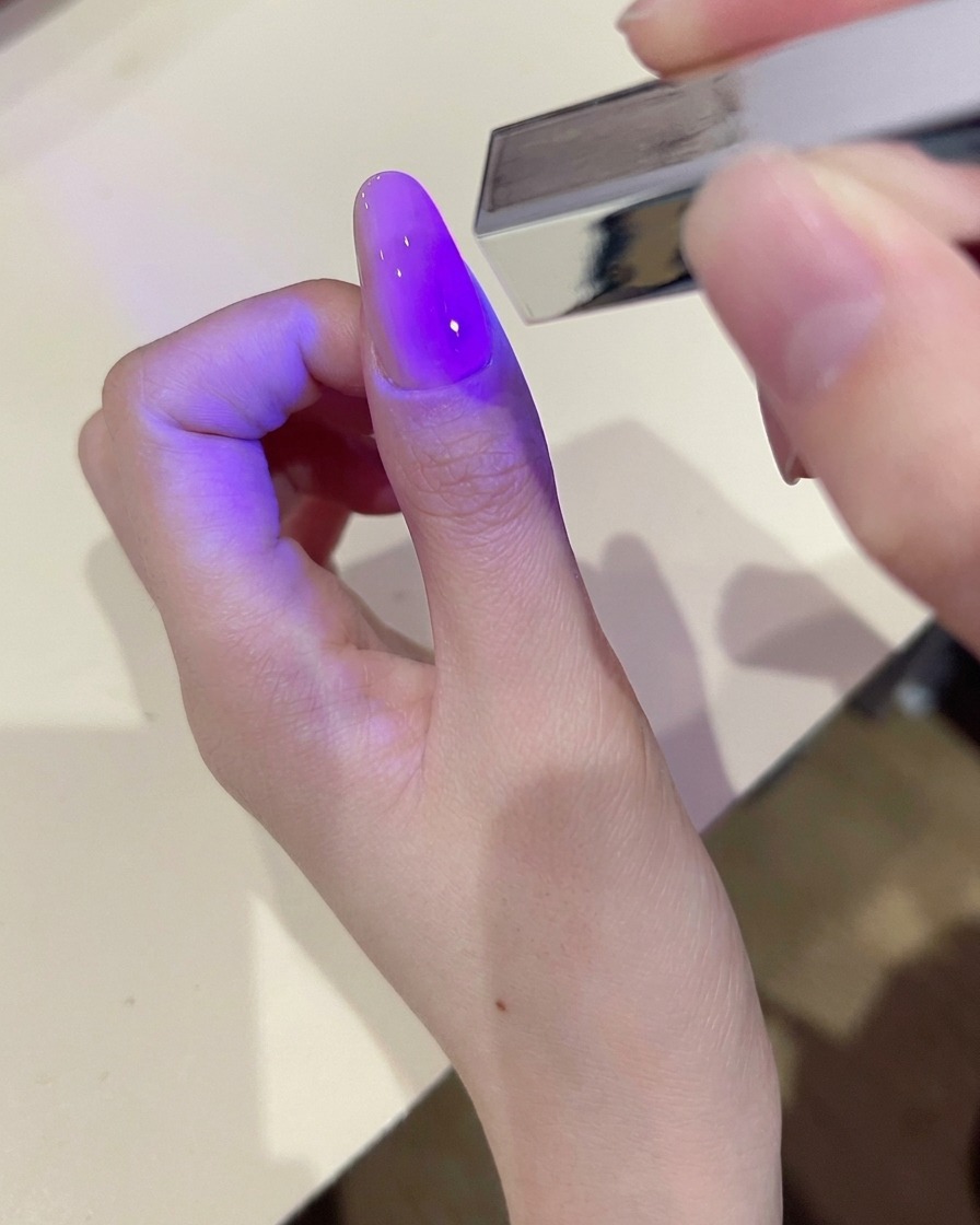 Una mano utilizando una toallita sin pelusa para limpiar la superficie de una uña de gel curada.