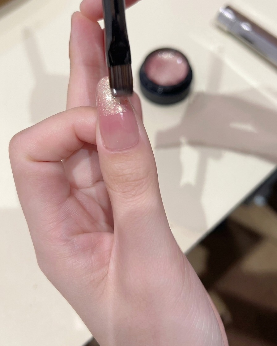 Un pincel de uñas pequeño aplicando gel cat eye en la punta de una uña, difuminándolo ligeramente hacia el centro.