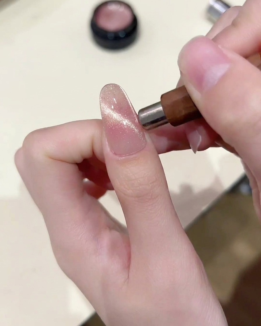 Una herramienta magnética sostenida paralela a la uña, concentrando las partículas de cat eye en una banda horizontal brillante.