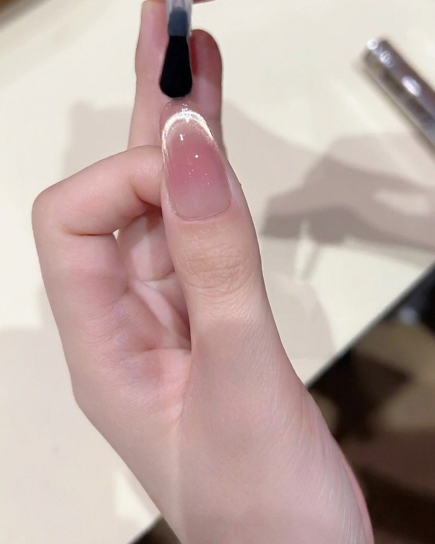 Un pincel aplicando una capa final de top coat de alto brillo sobre el diseño de uña cat eye terminado.