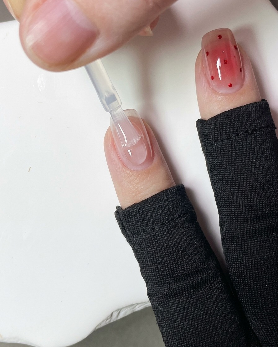 Primer plano de un puntero aplicando pequeños puntos de gel rojo sobre la superficie de una uña.