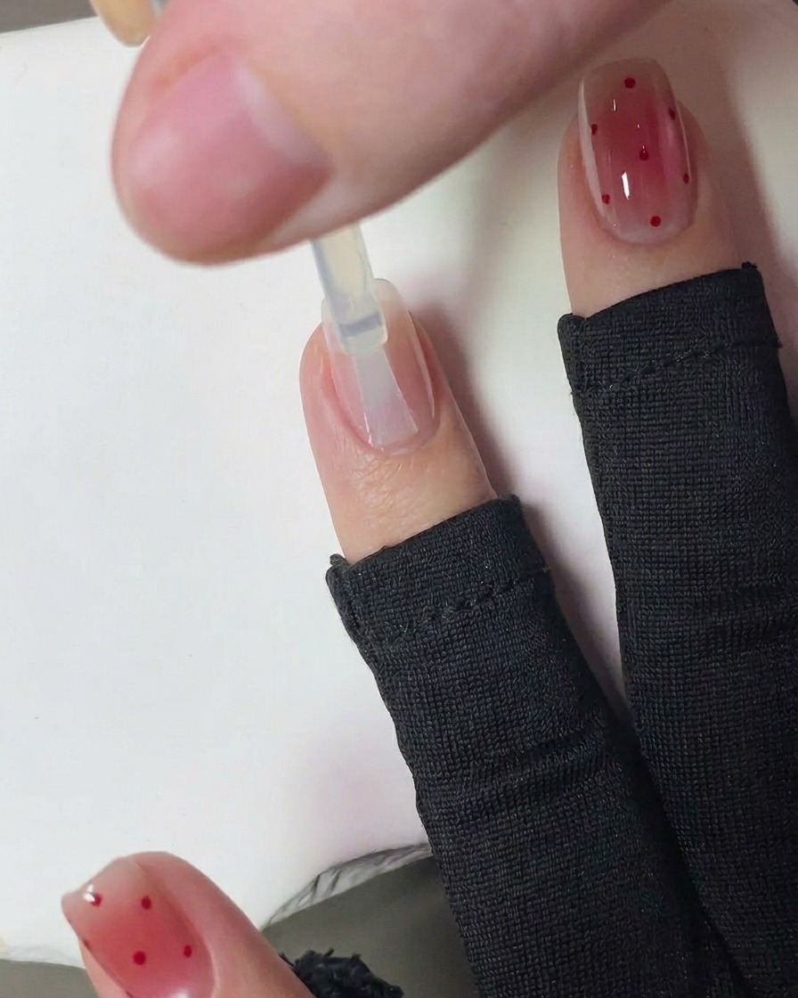 Una mano con uñas recién decoradas con lunares rojos curándose dentro de una lámpara UV de uñas.