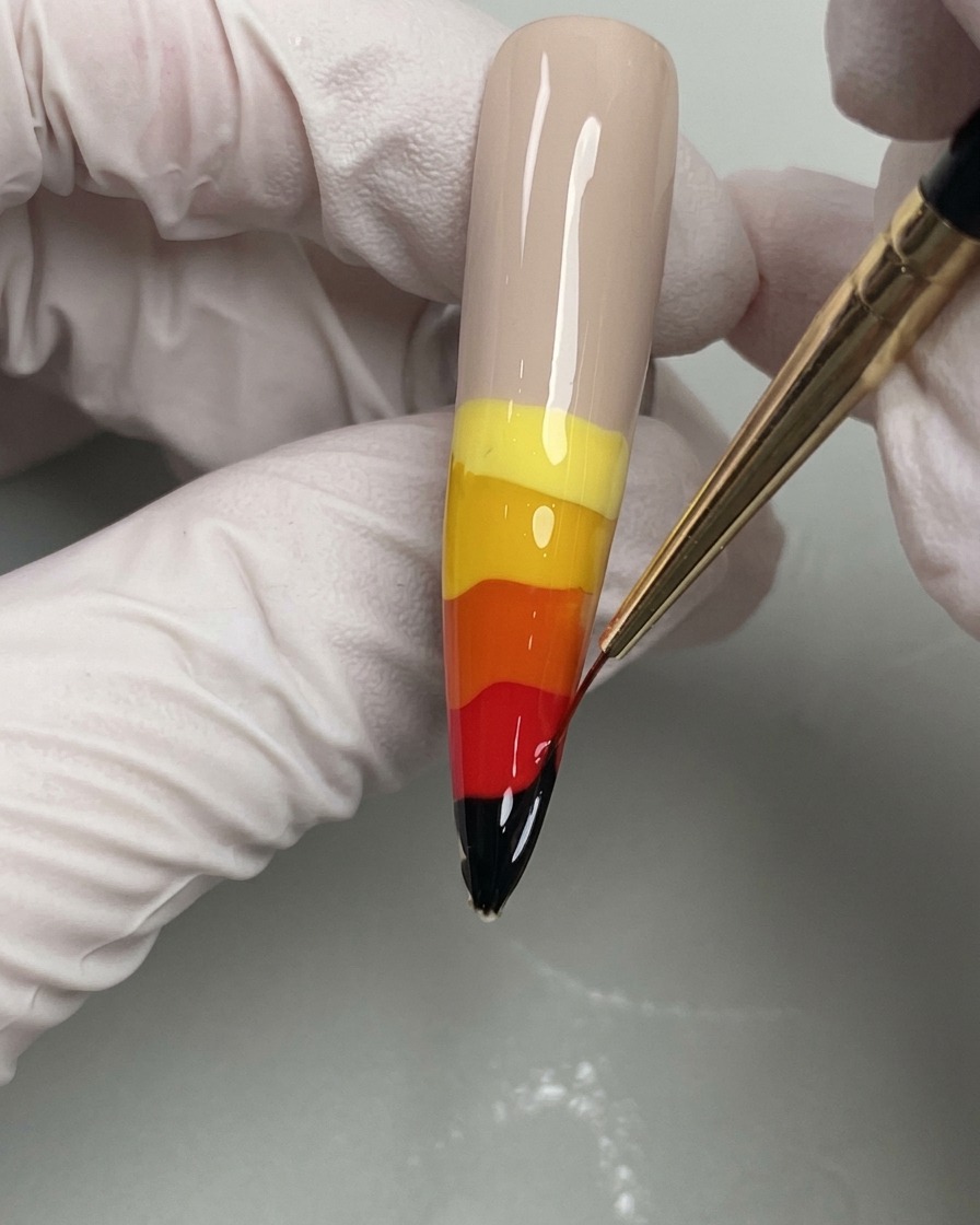 Un pincel delineador fino arrastrando colores de gel húmedos hacia arriba para crear llamas.