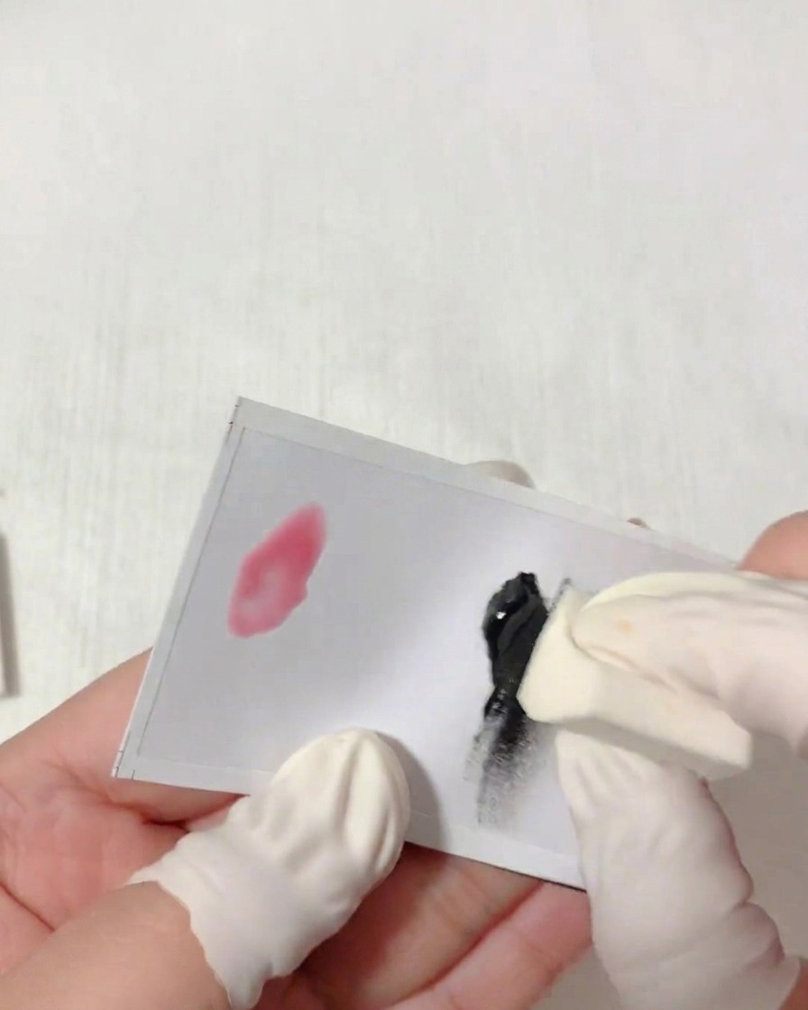 Primer plano de una mano con protector de dedo dando toques con una esponja triangular en gel negro sobre una paleta blanca.