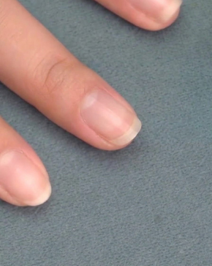 Un pincel aplicando esmalte de gel rosa translúcido sobre una uña natural limpia.