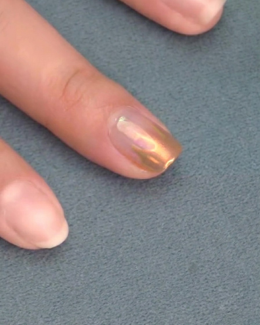 Un pincel aplicando un top coat transparente final sobre una uña con detalles cromados.