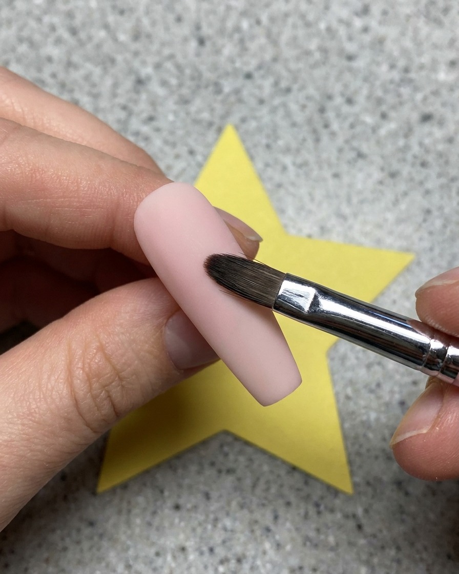 Primer plano de un gel transparente siendo aplicado con un pincel sobre una base de uña rosa.